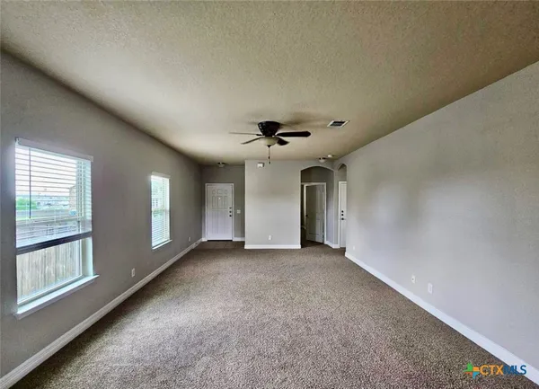 an empty room with chandelier fan and windows