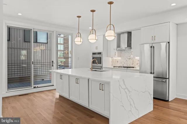 a large white kitchen with cabinets a island a refrigerator a stove a sink cabinets and wooden floor