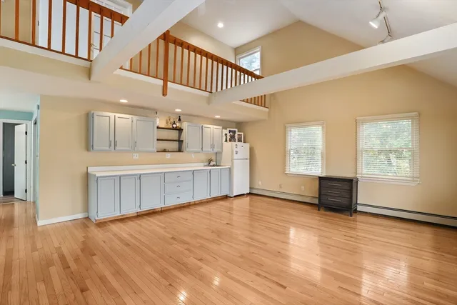 a view of an empty room with wooden floor and a kitchen