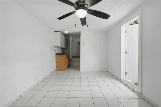 an empty room with wooden floor ceiling fan and kitchen space