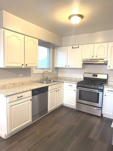 a white kitchen with granite countertop a stove and a sink