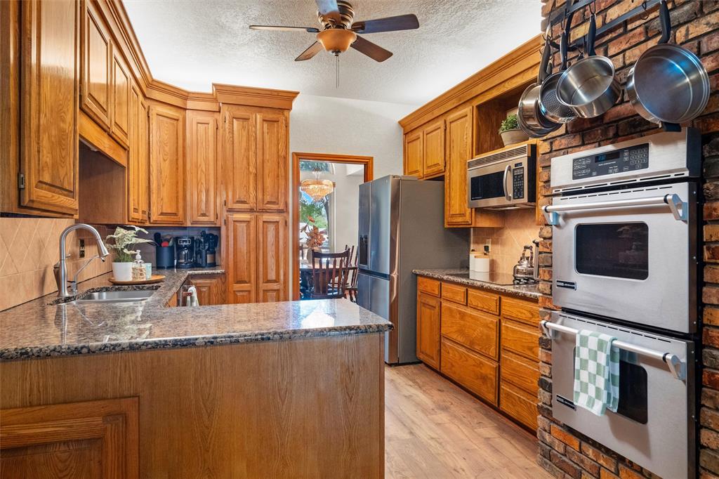 217 Valley Ranch Road Weatherford, TX 76087 - Photo 11 of 38 Kitchen featuring wood cabinetry, granite countertops, stainless steel appliances, a double wall oven, and a brick accent wall with a pot rack