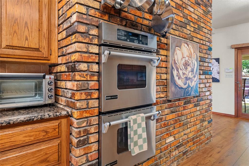 217 Valley Ranch Road Weatherford, TX 76087 - Photo 12 of 38 Exposed brick wall featuring stainless steel double wall ovens, wood-finish flooring, wood cabinetry, and a granite countertop