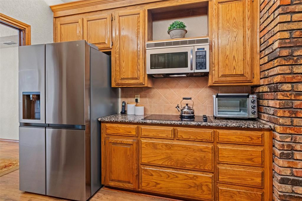 217 Valley Ranch Road Weatherford, TX 76087 - Photo 13 of 38 Kitchen area featuring wood cabinetry with crown molding, a stainless steel refrigerator, an integrated stovetop, and a brick accent wall