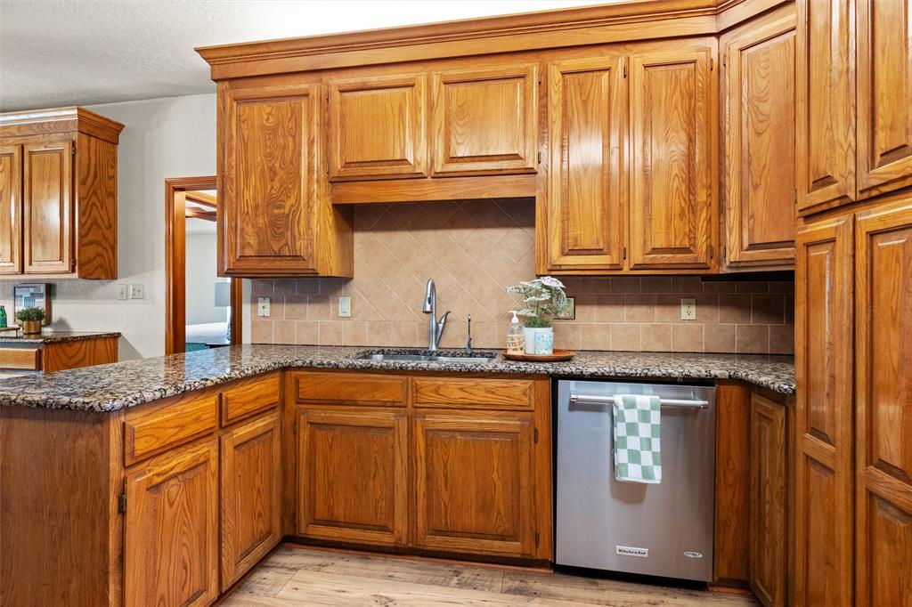 217 Valley Ranch Road Weatherford, TX 76087 - Photo 14 of 38 Kitchen featuring wood cabinetry with crown molding, stone countertops, a tile backsplash, and a stainless steel dishwasher