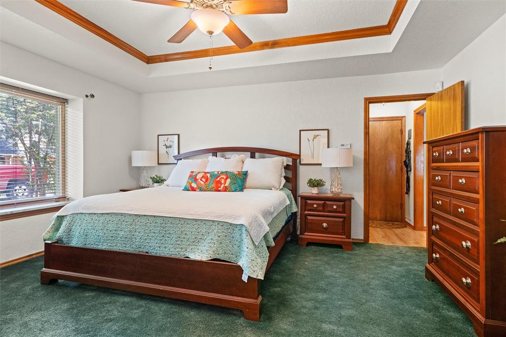 217 Valley Ranch Road Weatherford, TX 76087 - Photo 21 of 38 Bedroom featuring a tray ceiling with wood-finish trim, a ceiling fan with integrated lighting, window with blinds, and green carpeting