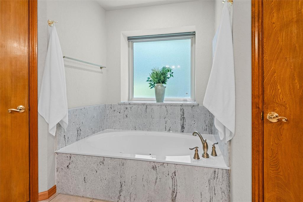217 Valley Ranch Road Weatherford, TX 76087 - Photo 25 of 38 Built-in soaking tub featuring a stone surround, bronze-finish fixtures, and a frosted window