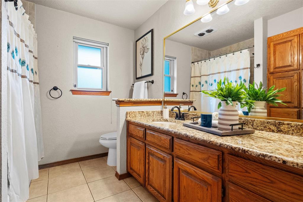 217 Valley Ranch Road Weatherford, TX 76087 - Photo 27 of 38 Bathroom vanity featuring a speckled countertop, dual undermount sinks with matte black faucets, and extensive wood cabinetry