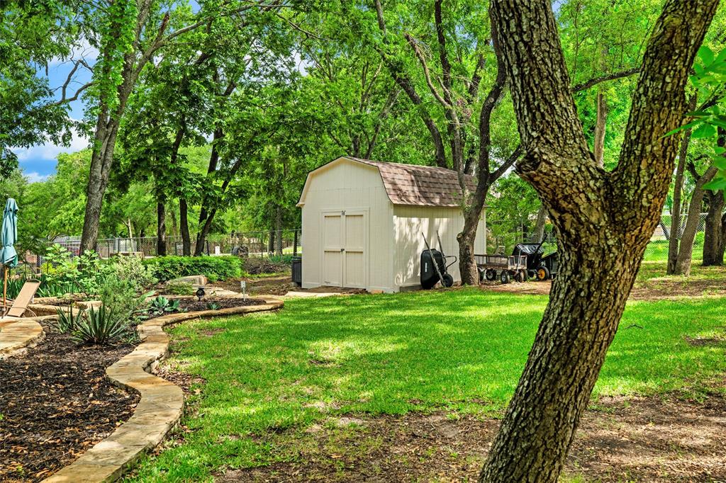 217 Valley Ranch Road Weatherford, TX 76087 - Photo 37 of 38 Expansive backyard featuring a storage shed with double doors, a manicured lawn, mature trees providing natural shade, and a stone-edged garden bed