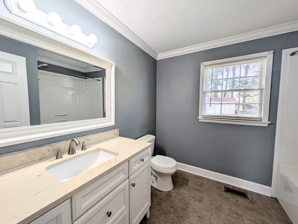 a bathroom with a granite countertop toilet a sink a mirror and a window