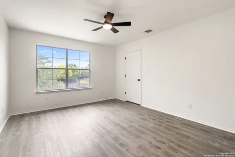 an empty room with wooden floor fan and windows