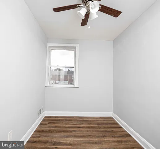an empty room with wooden floor chandelier fan and windows