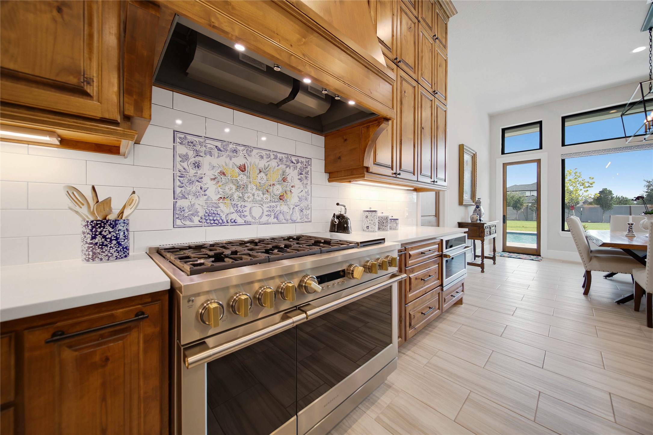 24718 Shadow Pond Spring, TX 77389 - Photo 15 of 49 Elegant kitchen featuring a high-end stainless steel gas range, beautiful wood cabinetry, and a charming tile backsplash, opening into a bright dining area with large windows overlooking the backyard.