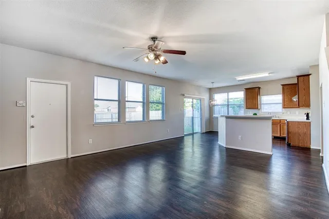 a view of an empty room with wooden floor and a kitchen