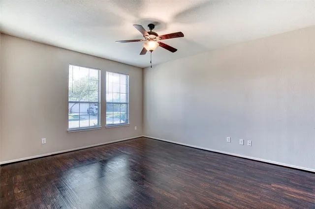 an empty room with wooden floor fan and windows