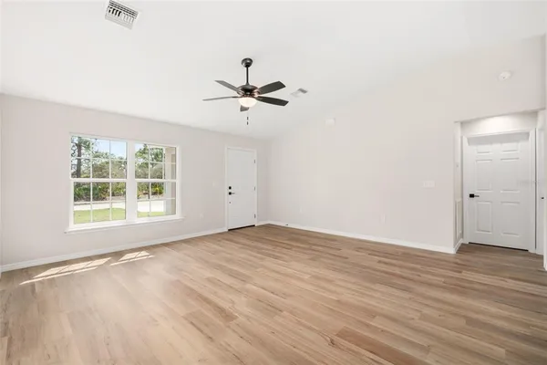 an empty room with wooden floor fan and windows