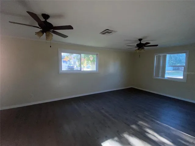 an empty room with wooden floor fan and windows