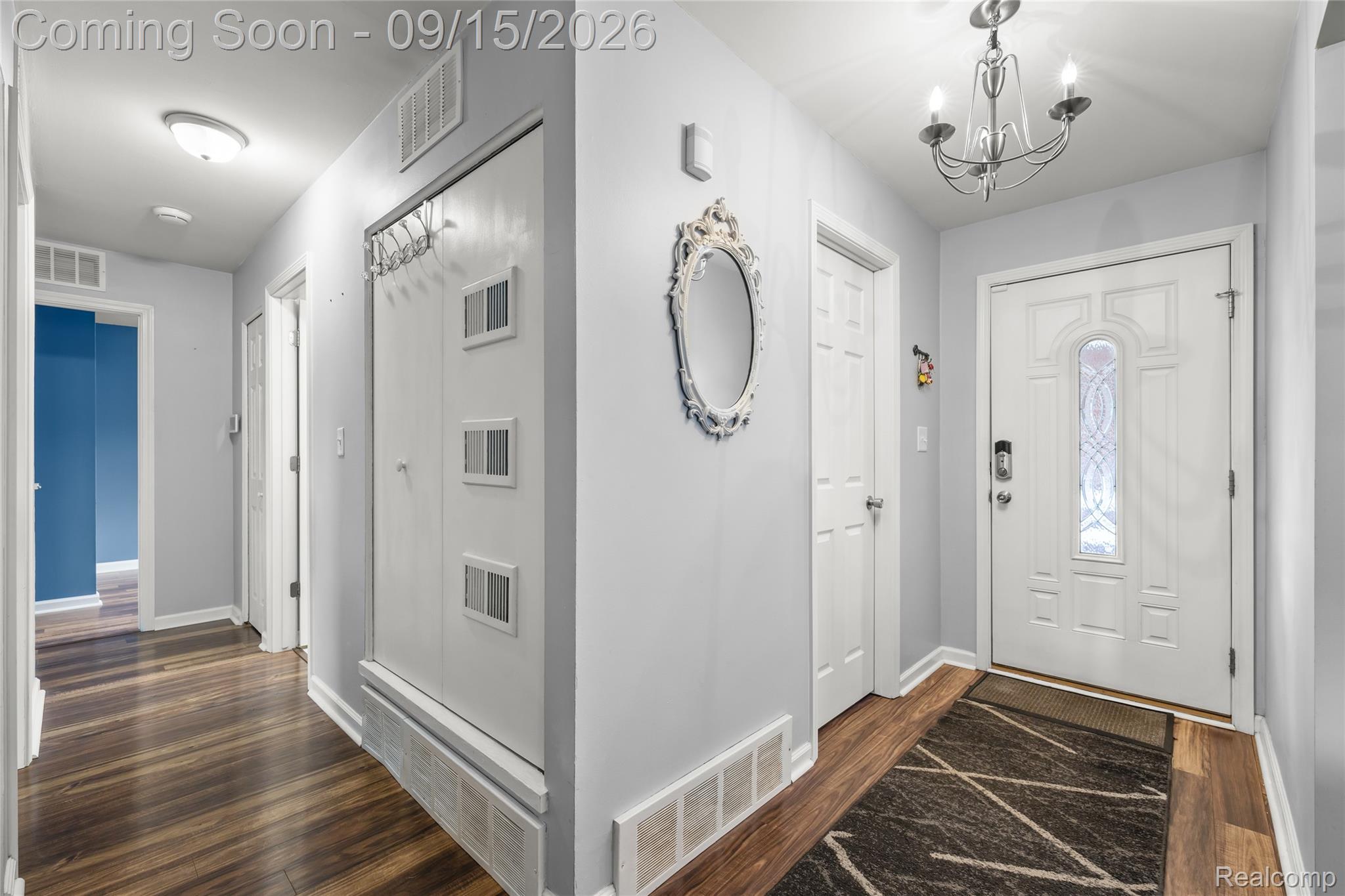 Entryway featuring a decorative front door with an ornate glass insert, wood-finish flooring, and a chandelier-style light fixture
