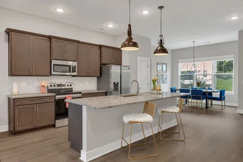 a kitchen with stainless steel appliances granite countertop a stove a sink a refrigerator a dining table and chairs