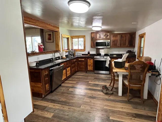 a kitchen with stainless steel appliances granite countertop a stove top oven a sink a dining table and chairs with wooden floor