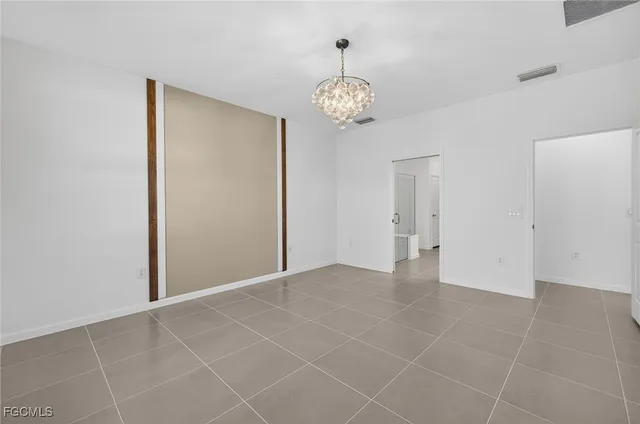 an empty room with a chandelier fan and kitchen view
