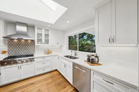 a kitchen with stainless steel appliances a stove a sink a refrigerator white cabinets and wooden floor