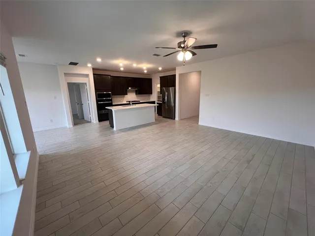 a view of an empty room with wooden floor and a ceiling fan