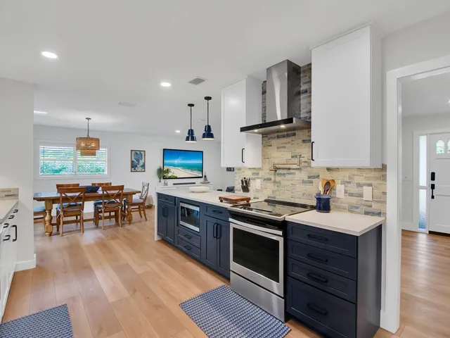 a kitchen with stainless steel appliances granite countertop a stove top oven a sink dishwasher and white cabinets with wooden floor