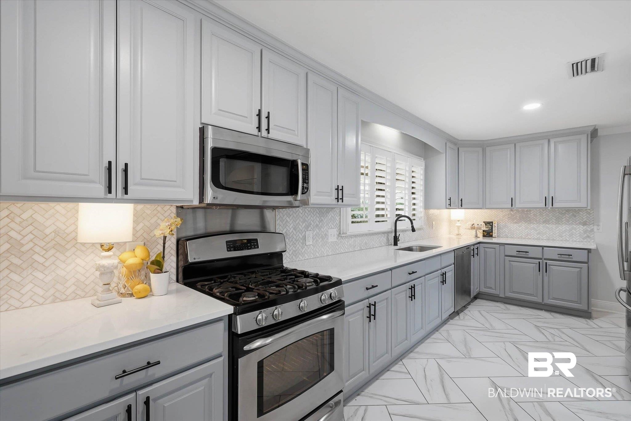3801 Point Road Mobile, AL 36619 - Photo 9 of 55 Modern kitchen featuring light gray cabinetry with black hardware, white countertops, stainless steel appliances, a herringbone tile backsplash, and patterned tile flooring