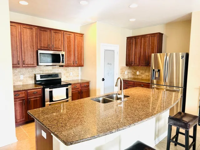 a kitchen with kitchen island granite countertop wooden cabinets refrigerator and microwave