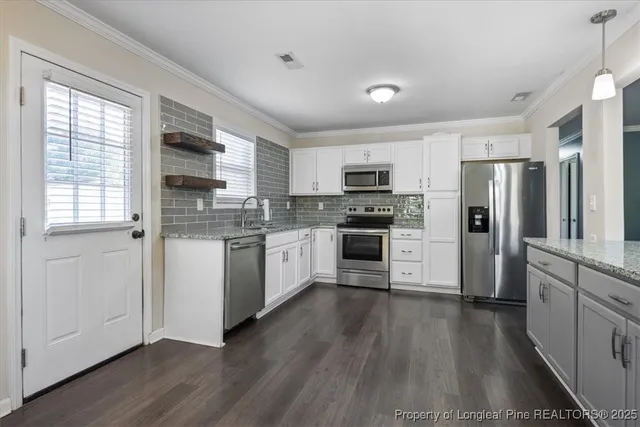 a kitchen with a white cabinets a sink a window a wooden floor and stainless steel appliances