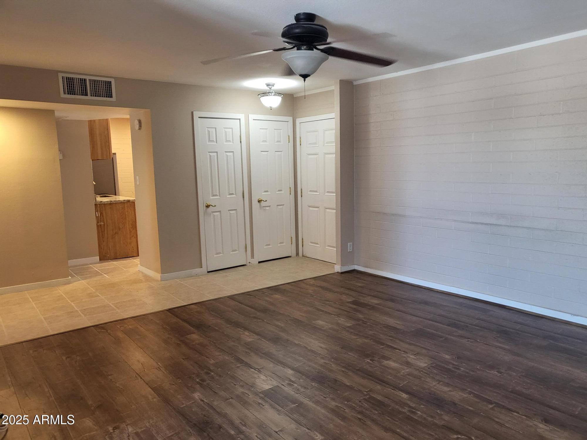 a view of an empty room with wooden floor and a ceiling fan