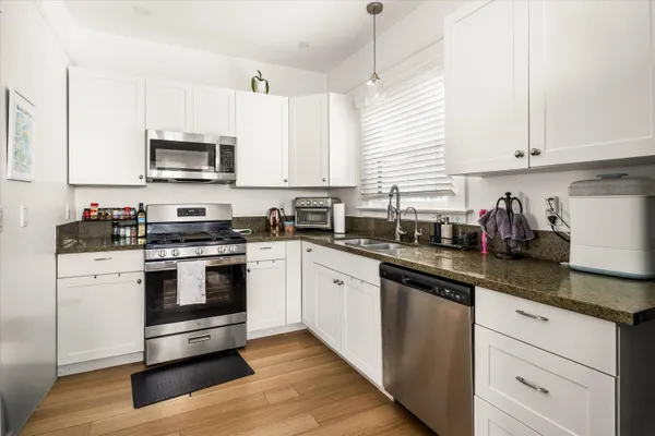 a kitchen with stainless steel appliances granite countertop white cabinets a sink a stove a microwave and wooden floors