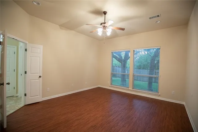 an empty room with wooden floor chandelier fan and windows