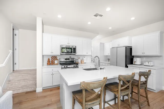 a kitchen with stainless steel appliances a dining table chairs refrigerator and microwave
