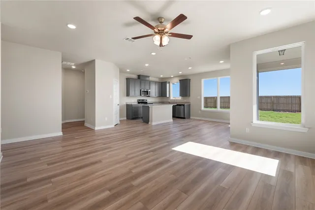 a view of an empty room with kitchen appliances and a ceiling fan