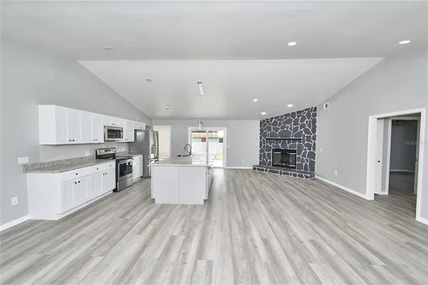a large white kitchen with kitchen island a stove a sink dishwasher and white cabinets with wooden floor