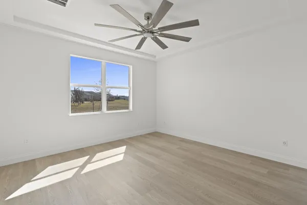 an empty room with wooden floor chandelier fan and windows