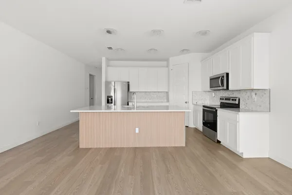 a living room with stainless steel appliances white cabinets a wooden floor and a sink