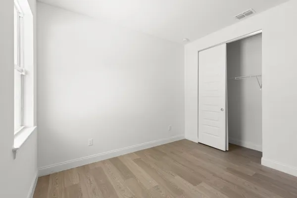 a view of an empty room with wooden floor and closet