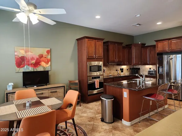 a kitchen with stainless steel appliances granite countertop a stove top oven a refrigerator a kitchen island a dining table and chairs with wooden floor