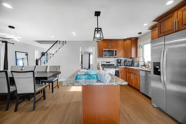 a kitchen with stainless steel appliances granite countertop a refrigerator a stove a sink dishwasher a dining table and chairs with wooden floor