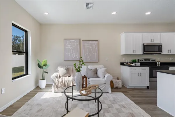 a kitchen with stainless steel appliances kitchen island granite countertop a refrigerator a stove a sink and white cabinets with wooden floor