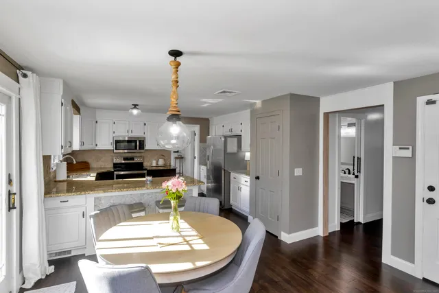 a kitchen with stainless steel appliances kitchen island granite countertop a refrigerator a stove a sink a dining table and chairs with wooden floor