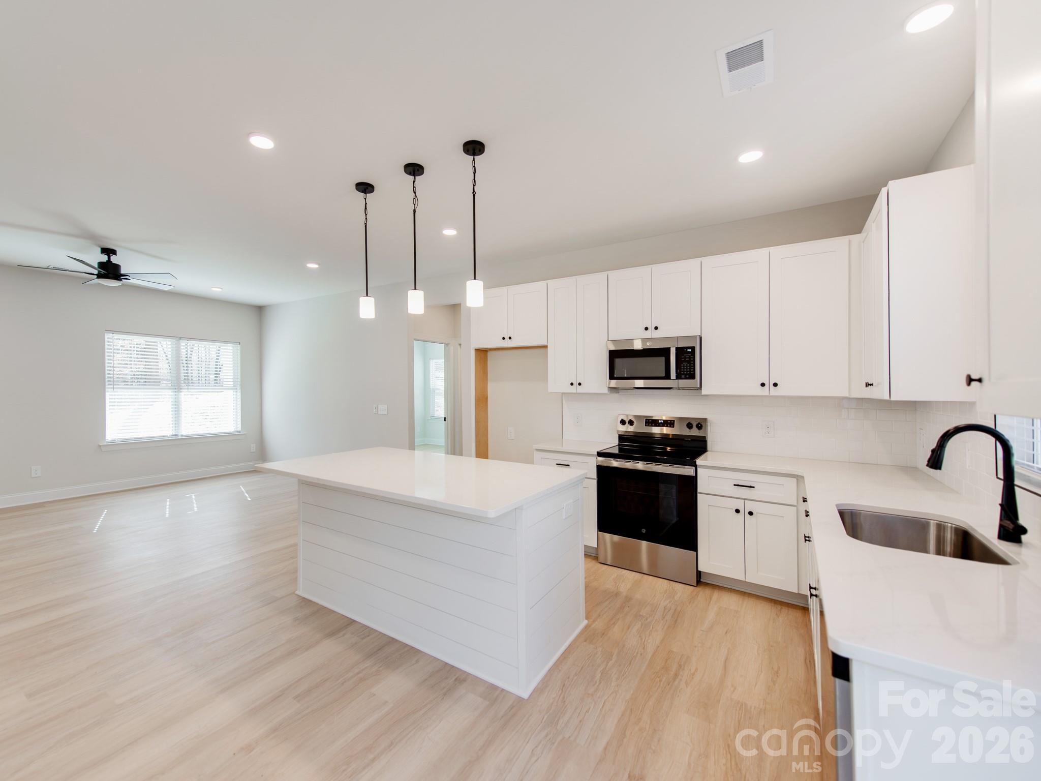 a large kitchen with stainless steel appliances kitchen island granite countertop a stove a sink a refrigerator and white cabinets with wooden floor