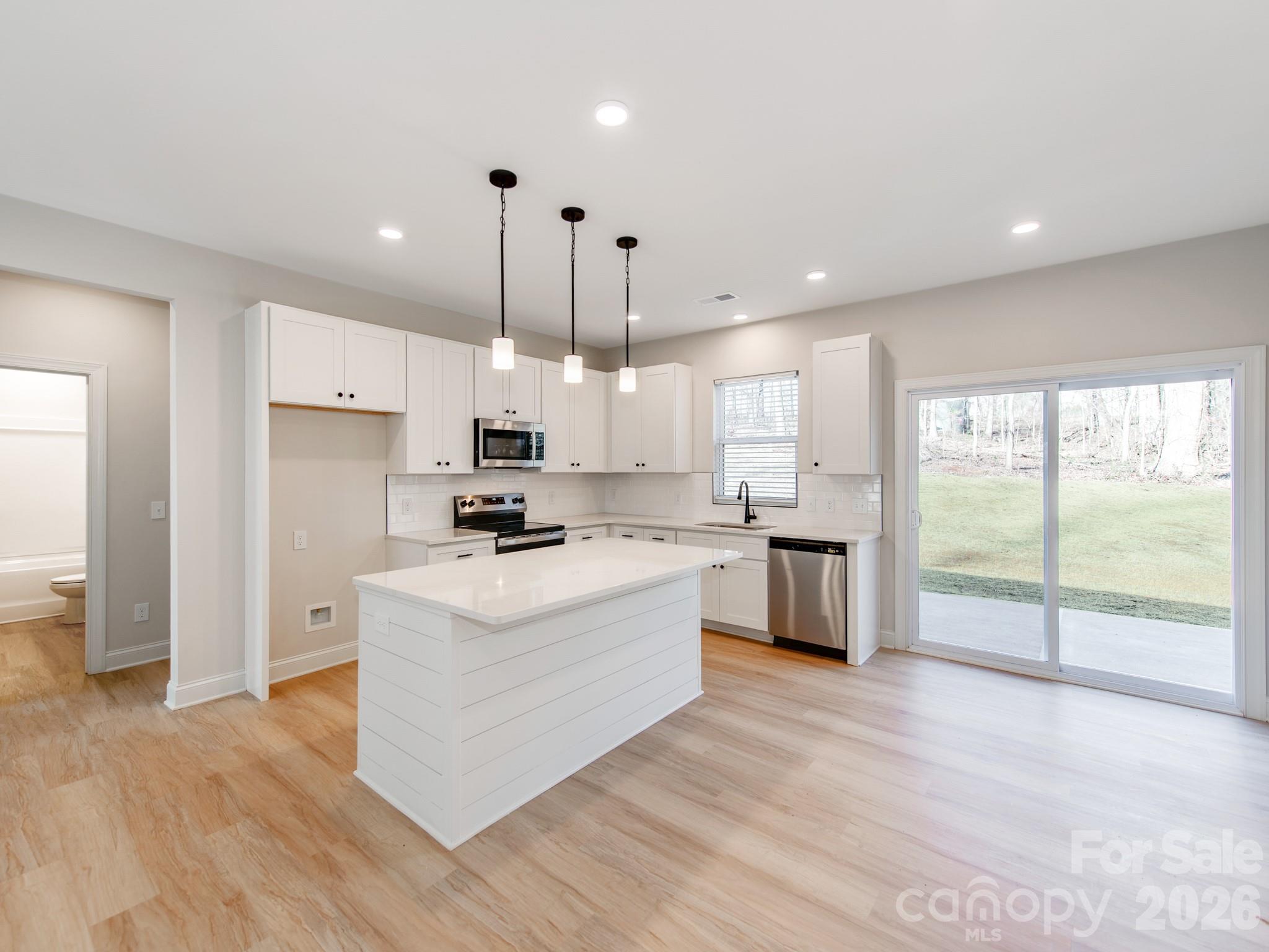 176 Whitetail Road Statesville, NC 28625 - Photo 2 of 23 a kitchen with kitchen island granite countertop a stove a sink a refrigerator white cabinets and wooden floor next to a window
