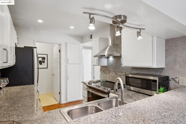 a kitchen with stainless steel appliances granite countertop a refrigerator a stove and a sink with wooden floor