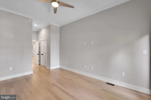 a view of an empty room with wooden floor and a ceiling fan