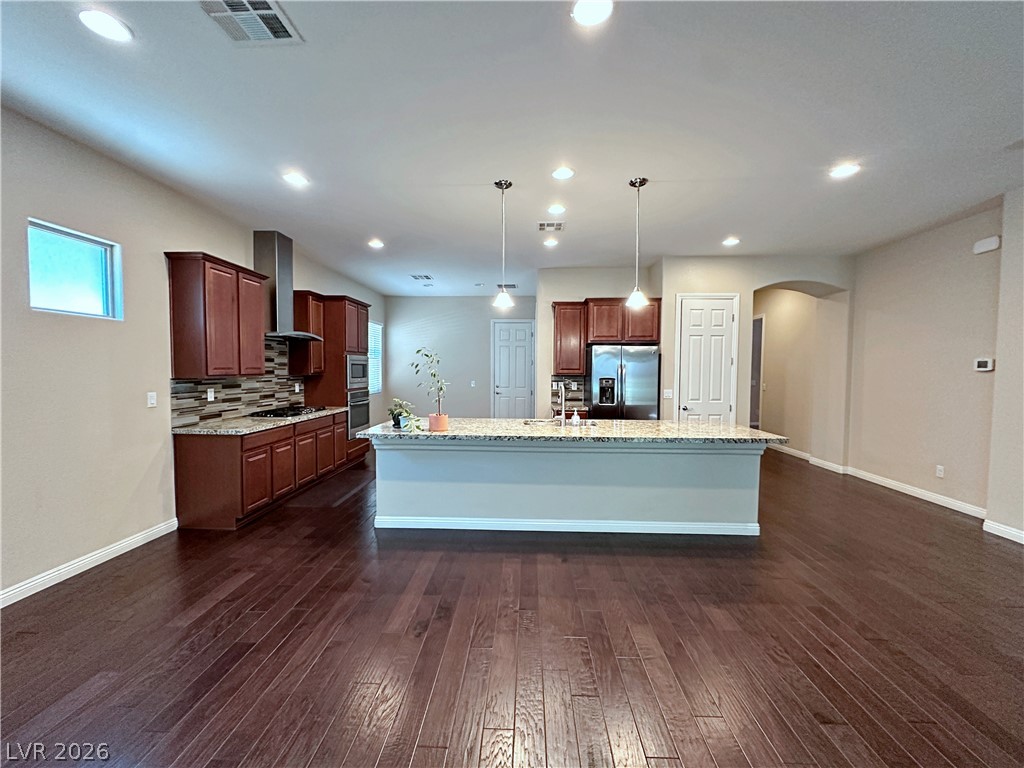 71 Newton Ridge Way Las Vegas, NV 89183 - Photo 12 of 40 An open-concept design connects the kitchen to a spacious living area, showcasing rich hardwood flooring and modern lighting.