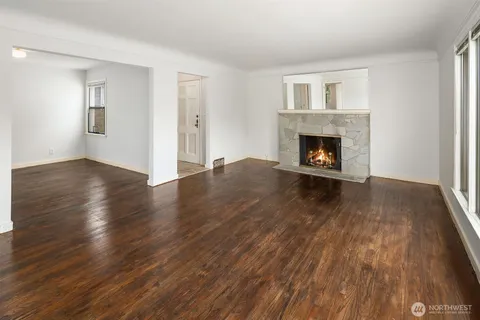 a view of an empty room with wooden floor fireplace and a window